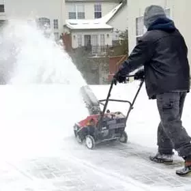 man pushing single stage snow blower on residential driveway