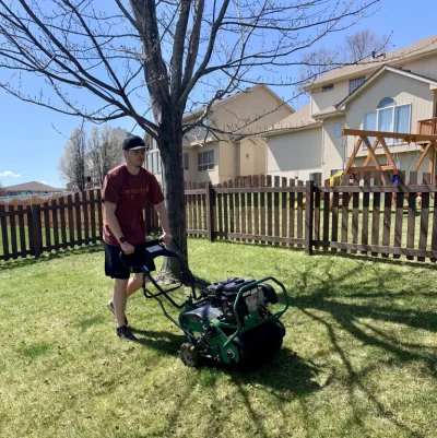 man pushing a core aeration machine over grass