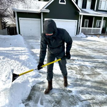 worker pushing snow with shovel, already cleared driveway behind